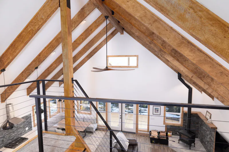 The great room of a custom timber-frame home above Kalispell, hand-hewn trusses under a vaulted ceiling, seen from the loft