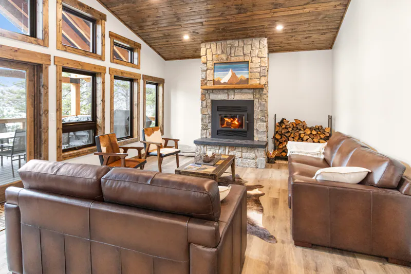 A wood-ceilinged great room with a lit stone fireplace in the Montana Lakefront Luxury Retreat