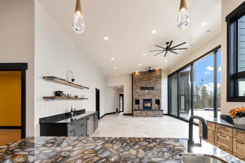 A Built Right kitchen and great room in Mountain Modern Living: an agate stone island, a floor to ceiling stone fireplace and a wall of glass to the pines