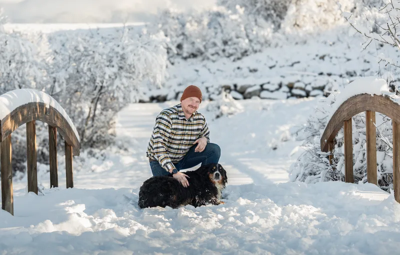 Zayne Davis kneeling in the snow with Bella, a Bernese mountain dog, between two snow-covered footbridges